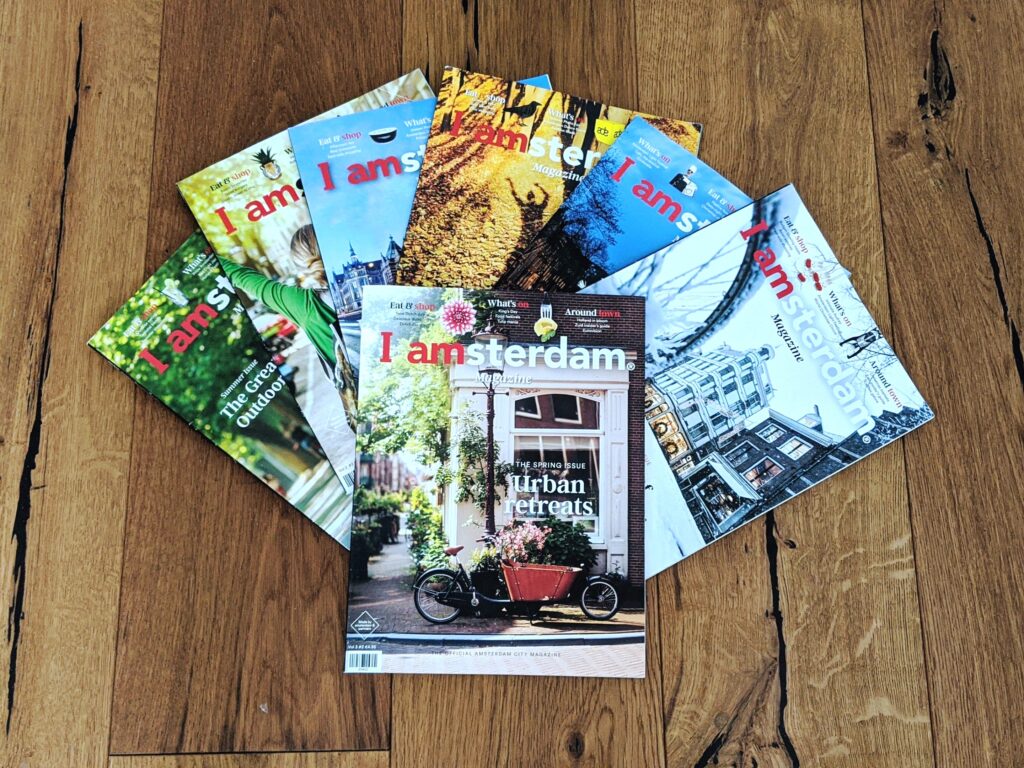 Issues of I amsterdam Magazine fanned out on a wooden table